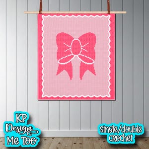 May include: A rectangular crochet wall hanging featuring a light pink center with a dark pink bow graphic in the middle. The piece is framed by a white scalloped border and hangs from a wooden rod. Text on the image reads KP Design Me Too.