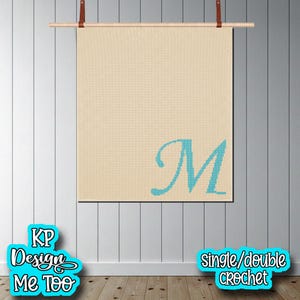 May include: A square beige crochet wall hanging featuring a large, centred, teal-coloured letter M in a cursive script font. The textile is suspended from a horizontal wooden rod with brown leather straps attached to the top corners.
