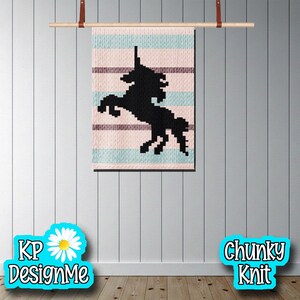 Puede incluir: Un tapiz de pared de punto grueso con una silueta de unicornio negro sobre un fondo a rayas rosa, azul y marrón. Colgado de una barra de madera con correas de cuero. El texto "KP DesignMe" y "Chunky Knit" está en la imagen.