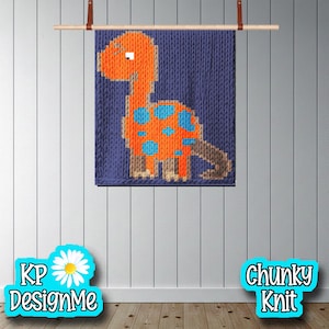 Peut inclure: Une tenture murale en tricot épais représentant un dinosaure orange à pois bleus sur fond bleu. Le dinosaure est suspendu à une tringle en bois avec des lanières en cuir. Les textes "KP DesignMe" et "Chunky Knit" sont visibles.