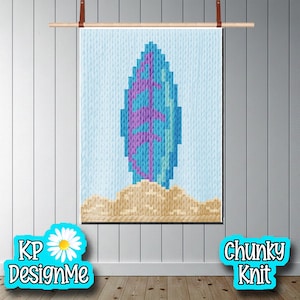 May include: A chunky knit wall hanging featuring a surfboard design in shades of blue and purple, resting on a sandy base. The artwork is displayed on a light blue background and includes the text "KP DesignMe" and "Chunky Knit".