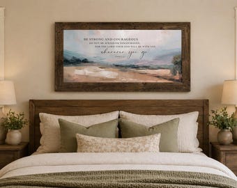 Könnte beinhalten: Ein gerahmter Landschaftskunst-Druck mit Holzrahmen hängt über einem Bett. Das Kunstwerk zeigt eine weiche Farbpalette aus Blau-, Grün- und Beigetönen. Der Text lautet: "SEI STARK UND MUTIG... wohin du auch gehst."