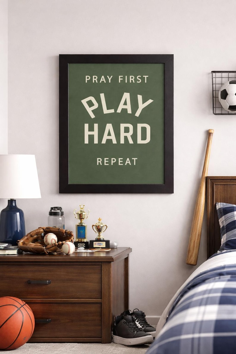 Black color frame of a Christian sports framed wall art with the phrase Pray First Play Hard Repeat on a green background in a vertical layout. Pictured in a boys room.