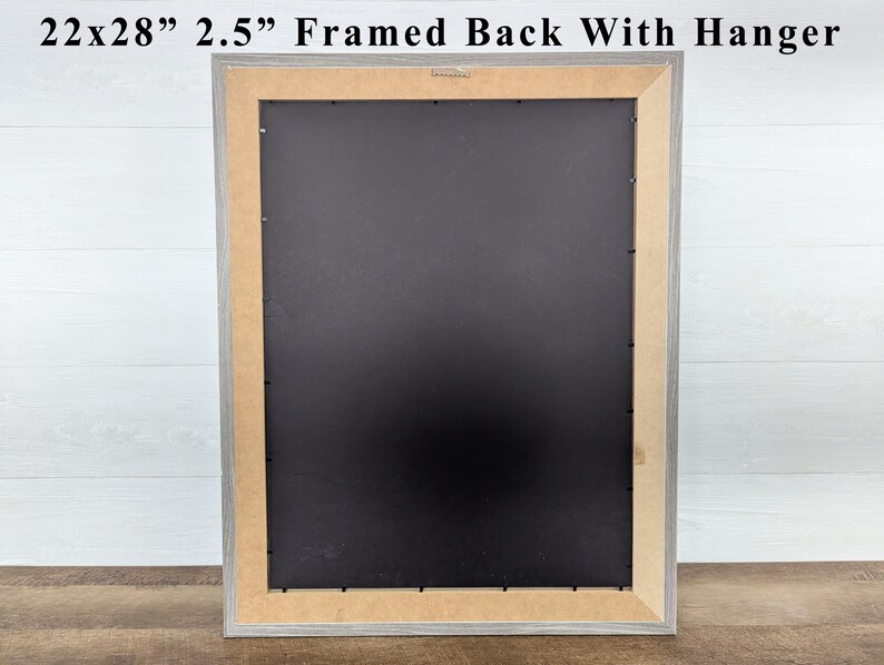 May include: A framed artwork back with a hanger. The frame is 22x28 inches and 2.5 inches wide. The frame is gray with a black backing and a light brown interior border. The text at the top reads: 22x28" 2.5" Framed Back With Hanger.