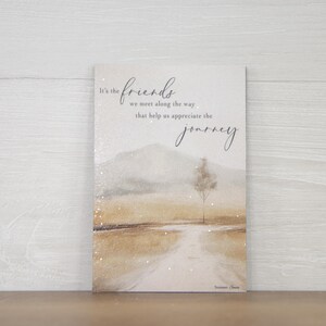 May include: A rectangular greeting card with a landscape painting. The artwork features a road leading to a tree and mountains, with text that reads "It's the friends we meet along the way that help us appreciate the journey."