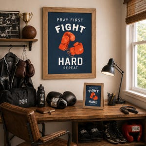 May include: A framed wall poster and a smaller desk frame both featuring the text PRAY FIRST FIGHT HARD REPEAT with an illustration of two orange boxing gloves on a dark blue background. The scene includes boxing gear like gloves and a headguard.