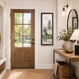 May include: A vertical rectangular wall sign with a dark wood frame featuring a watercolor painting of pine trees, a lake, and the text I CAN DO ALL THINGS THROUGH CHRIST. The sign is mounted on a white wall next to a wooden door and a console table.