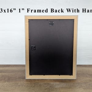 May include: The back of a framed artwork, with a black backing and a natural wood-tone frame. The frame is 13x16 inches and 1 inch thick, with a hanger attached. The text "13x16" 1" Framed Back With Hanger" is visible at the top.