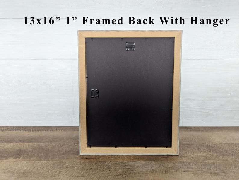 May include: The back of a framed artwork, with a black backing and a natural wood-tone frame. The frame is 13x16 inches and 1 inch thick, with a hanger attached. The text "13x16" 1" Framed Back With Hanger" is visible at the top.