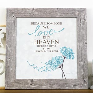 May include: A framed print with a white background and blue dandelion-like flowers. The text reads "Because someone we love is in heaven, there is a little bit of heaven in our home."