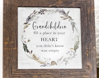 May include: A framed print with a watercolor wreath of leaves and flowers. The text reads "Grandchildren fill a place in your HEART you didn't know was empty".