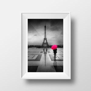 Könnte beinhalten: Ein Schwarzweißfoto des Eiffelturms in Paris, Frankreich. Eine Person steht im Vordergrund und hält einen leuchtend pinkfarbenen Regenschirm. Der Boden ist nass und reflektierend.