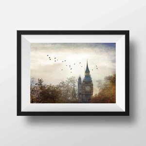 Puede incluir: Una fotografía enmarcada del Big Ben en Londres, Inglaterra. La torre del reloj está parcialmente oculta por árboles en primer plano. Una bandada de pájaros vuela por encima en el cielo.