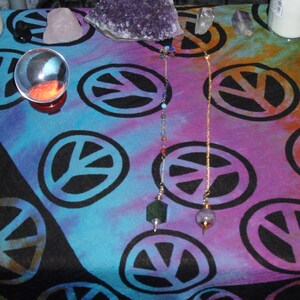 May include: A close-up of a crystal ball on a table with a tie-dye tablecloth. The tablecloth has a peace sign pattern and the crystal ball is surrounded by two pendulums with crystals at the end.