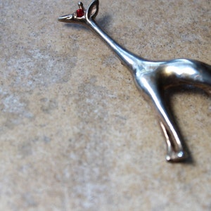 May include: A silver giraffe brooch with a red rhinestone eye.
