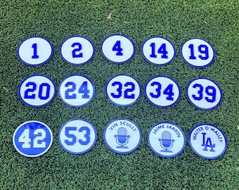 May include: A set of 12 round, white, blue-rimmed, baseball-themed patches with numbers and names. The patches include numbers 1, 2, 4, 14, 19, 20, 24, 32, 34, 39, 42, and 53. The patches also include the names "Vin Scully", "Jaime Jarrin", and "Walter O'Malley".