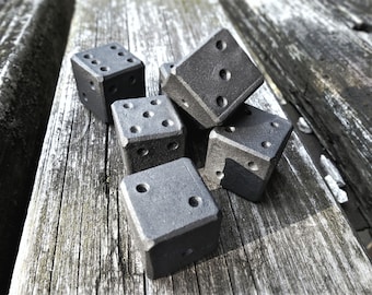May include: Six black metal dice with rounded edges, lying on a weathered wooden surface.