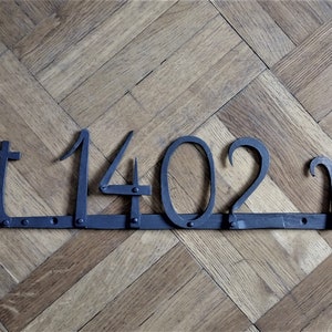 May include: A dark metal sign with the text "alt 1402 m" displayed on a wooden floor. The numbers and letters are crafted in a stylized font, with the "m" at the end. The sign is attached to a wooden base.