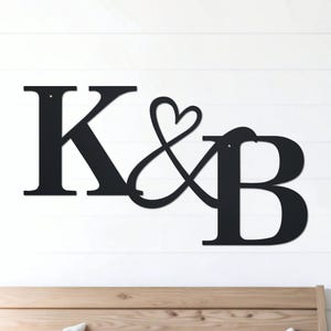 May include: Black metal wall decor with the letters K & B intertwined with a heart symbol.