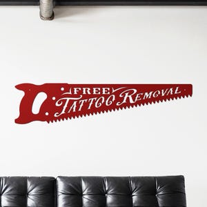 Sign shaped like a handsaw with the words Free Tattoo Removal cut out of it. Powder coated in a gloss red powder coat.