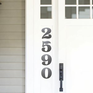 May include: Black metal house numbers 2590 are attached to a white door. The numbers are in a vertical line.