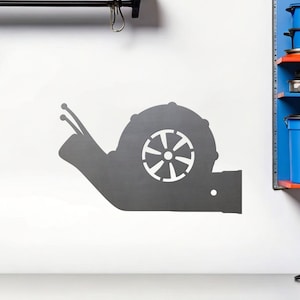 May include: A gray metal wall decal of a snail with a turbocharger shell. The snail is facing right and has two antennas.