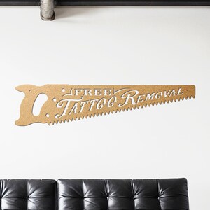 Sign shaped like a handsaw with the words Free Tattoo Removal cut out of it. Powder coated in a gold powder coat.