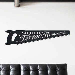 Sign shaped like a handsaw with the words Free Tattoo Removal cut out of it. Powder coated in a matte black powder coat.