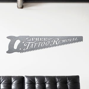 Sign shaped like a handsaw with the words Free Tattoo Removal cut out of it. Powder coated in a metallic silver powder coat.