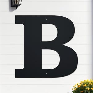 May include: Black metal letter B, mounted on a white wall. The letter is large and has a simple, modern design.