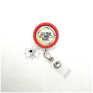 May include: Red retractable badge holder with a round, white, glitter-covered cap featuring a rainbow progress bar and the text "Gay Pride Loading..."