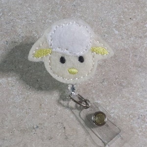 May include: White felt lamb with yellow ears and black eyes, attached to a clear plastic badge holder with a silver retractable reel.