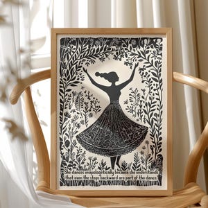 May include: A framed black and white art print featuring a silhouette of a dancing figure with arms raised. The figure is surrounded by floral and botanical elements. The print includes the quote: "She dances unapologetically because she understands that even the steps backward are part of the dance."