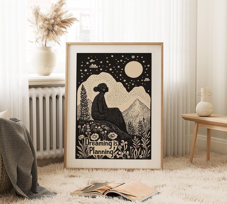 May include: Black and white illustration of a person sitting on a hilltop under a starry night sky with a full moon. The text "Dreaming is Planning" is below the person.