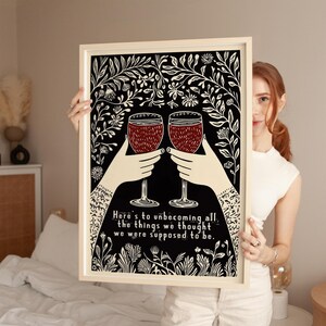 May include: A black and white print with a floral design and two wine glasses clinking. The text reads "Here's to unbecoming all the things we thought we were supposed to be."