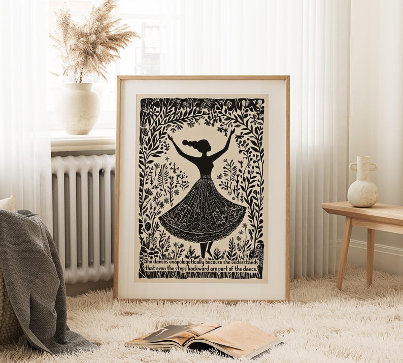 May include: A framed art print featuring a black silhouette of a dancing figure with arms raised. The figure is surrounded by floral and botanical elements. The print includes the text: "She dances unapologetically because she understands that even the steps backward are part of the dance."