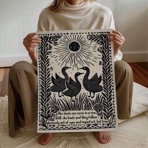 以下が含まれることがあります： 黒と白のアートプリント。3羽のアヒルが太陽の光の下に描かれています。プリントには「Her ducks are never in a row. Still, she leads and they follow - gloriously out of sync and imperfect, but true.」というテキストが含まれています。