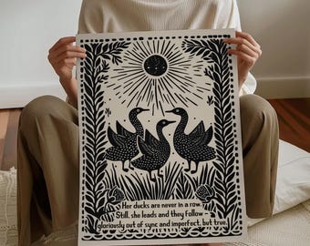 Könnte beinhalten: Schwarz-Weiß-Kunstdruck mit drei stilisierten Enten unter einem Sonnenstrahl-Design. Der Druck enthält den Text: "Her ducks are never in a row. Still, she leads and they follow - gloriously out of sync and imperfect, but true."