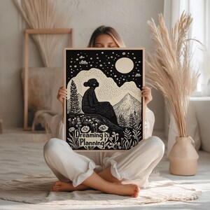 May include: Black and white illustration of a person sitting on a hill with a full moon and stars in the sky. The text "Dreaming is Planning" is at the bottom of the image.