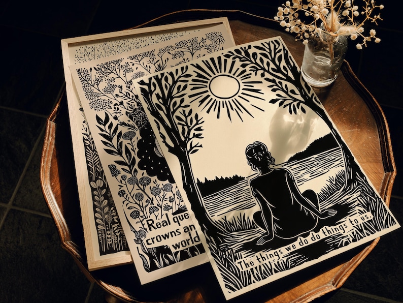 May include: Black and white art prints featuring nature-inspired designs and text. One print shows a figure by a lake with the text "The things we do do things to us." Another print has the text "Real que crowns an world."