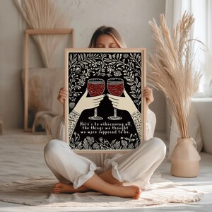 May include: Black and white illustration of two wine glasses with red wine, surrounded by floral designs. The text reads "Here's to unbecoming all the things we thought we were supposed to be."
