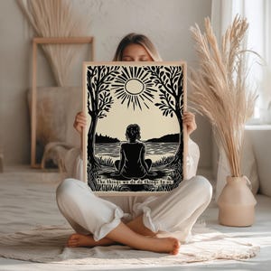 May include: A framed art print featuring a black and cream-colored illustration of a person sitting by a lake, with trees and a sun in the background. The text "The things we do do things to us" is at the bottom.