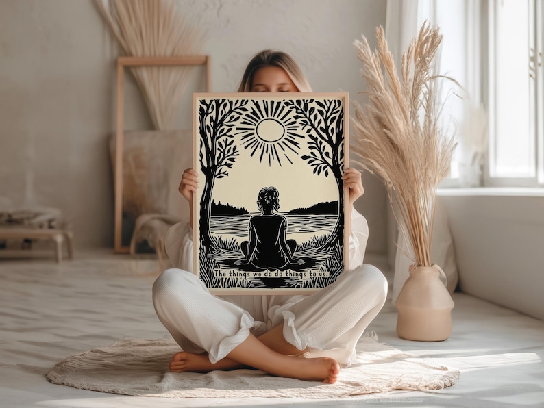 May include: A framed art print featuring a black and cream-colored illustration of a person sitting by a lake, with trees and a sun in the background. The text "The things we do do things to us" is at the bottom.