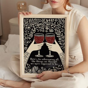 May include: A black and white print with a floral design and two wine glasses clinking. The text reads "Here's to unbecoming all the things we thought we were supposed to be."