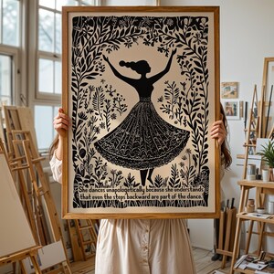 May include: A framed black and white art print featuring a silhouette of a dancing figure in a floral setting. The print includes the text: "She dances unapologetically because she understands that even the steps backward are part of the dance."