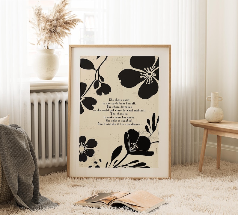 Puede incluir: Una impresi&oacute;n art&iacute;stica enmarcada con un fondo beige, motivos florales negros y texto. El texto dice "She chose quiet...Don't mistake it for compliance." La obra de arte se exhibe en una habitaci&oacute;n con un jarr&oacute;n de flores secas y un libro.