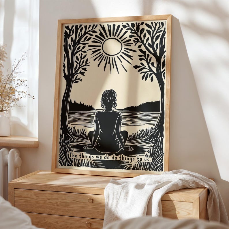 May include: A framed art print featuring a black and beige illustration of a person sitting by a lake, with trees and a sun in the background. The text "The things we do do things to us." is at the bottom.