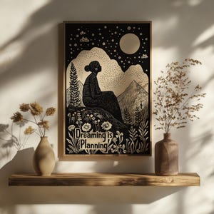 May include: Black and white illustration of a person sitting on a hilltop under a crescent moon and stars. The text "Dreaming is Planning" is below the person.