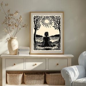 May include: Black and white art print in a wooden frame. The artwork depicts a person sitting by a lake, framed by trees and a sun. The text at the bottom reads, "The things we do do things to us."