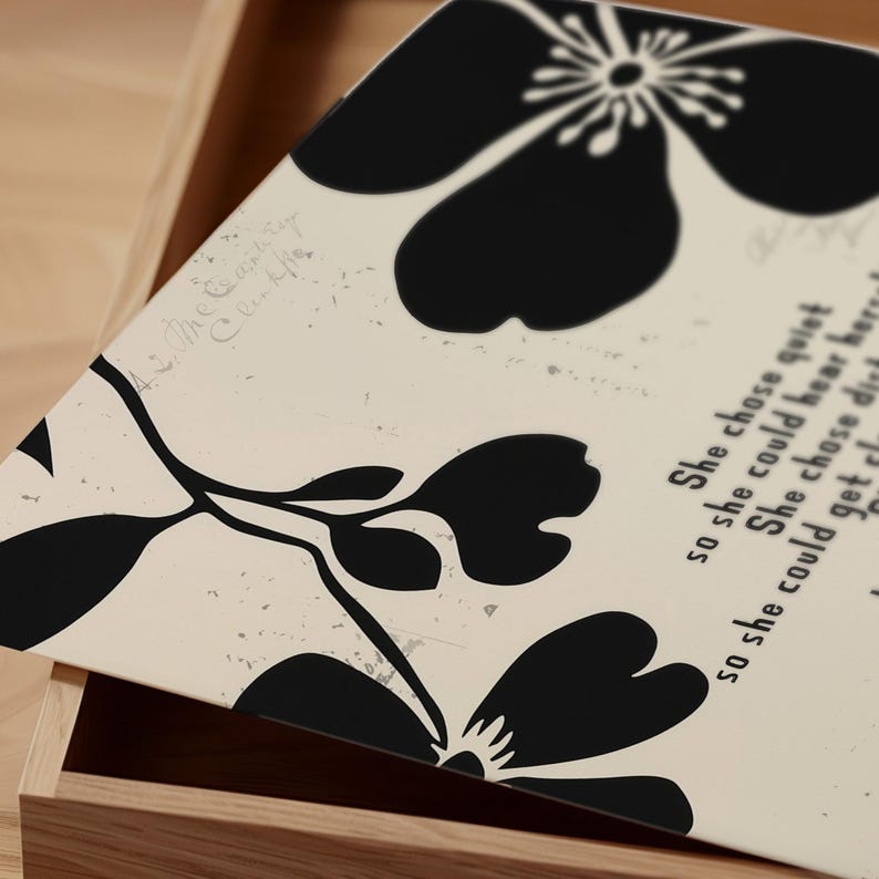 Puede incluir: Un objeto rectangular con un dise&ntilde;o floral en blanco y negro. El dise&ntilde;o presenta grandes flores y hojas estilizadas sobre un fondo color crema. El texto "She chose quiet" es visible en el lado derecho del objeto.
